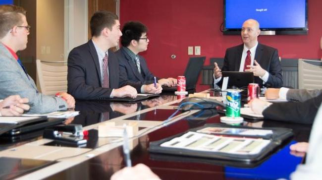 Students sit around a table with a business professional